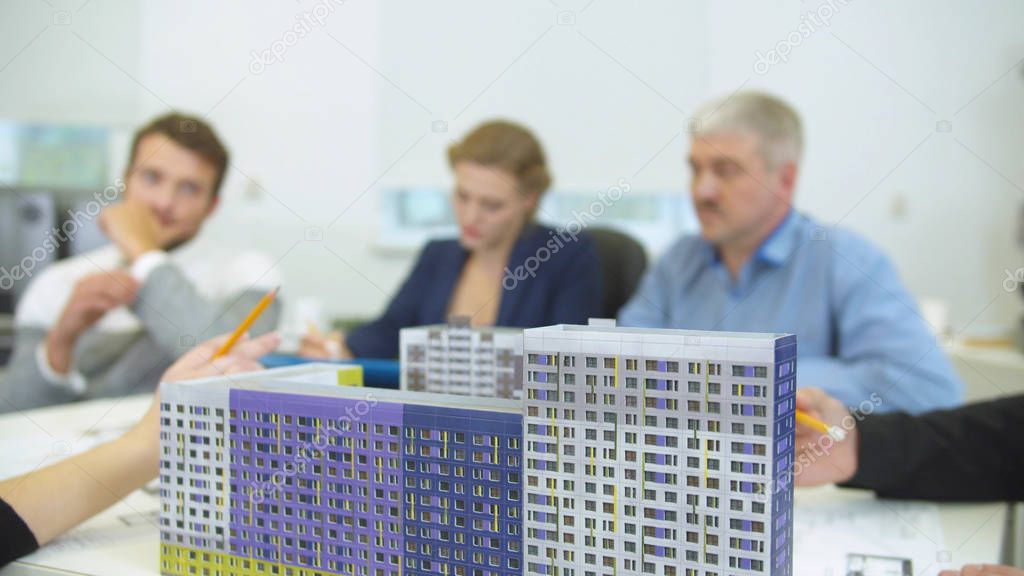 Focus on model of houses, people work on the background