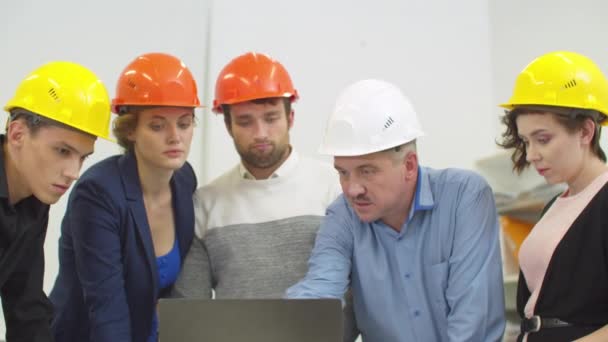 Workmates in helmets stands and listen to the talking man, who shows something on laptop — ストック動画