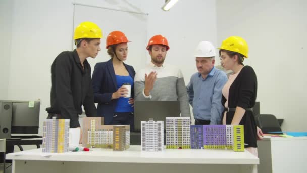 People in helmets discuss a project and models of houses — ストック動画