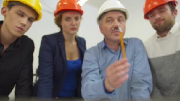 Compañeros de trabajo escuchan al arquitecto en el casco mostrando un esquema en la pantalla de la computadora portátil — Vídeos de Stock