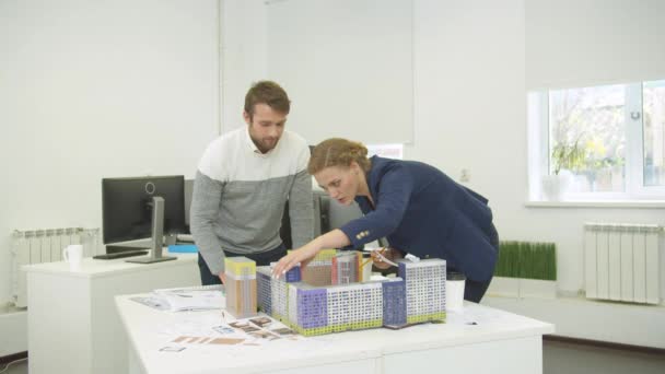 기술자들은 설계 도면을 보고 식탁 위에 집들의 모형을 세운다 — 비디오