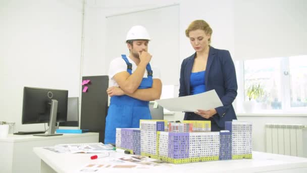 Žena stojí se stavitelem a ukazuje něco na modelu domu — Stock video