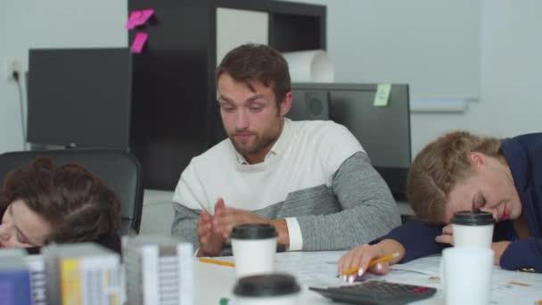 El hombre cansado se sienta en una mesa y aplaude para seguir trabajando — Vídeos de Stock