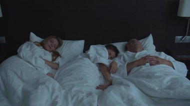 Ailesi otelde, oğlu bir yatakta anne babasıyla yatıyor.