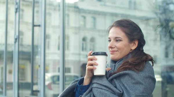 A lány szürke takaróba burkolózik, és kávét iszik egy kávézóban. — Stock Fotó