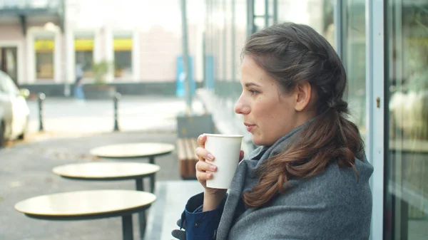 Oldalnézet, fiatal nő becsomagolja magát egy szürke takaróba és kávét iszik. — Stock Fotó
