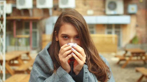 A szürke takarós lány forró teát iszik, és a kamerába néz. — Stock Fotó