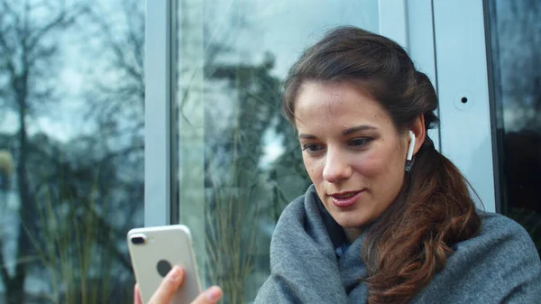Chica en auriculares sentarse en la calle y hablar por teléfono —  Fotos de Stock