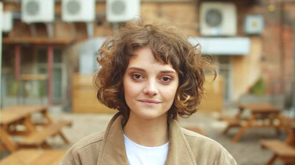 Kız sokakta durur, çay içer ve gülümseyerek kameraya bakar.