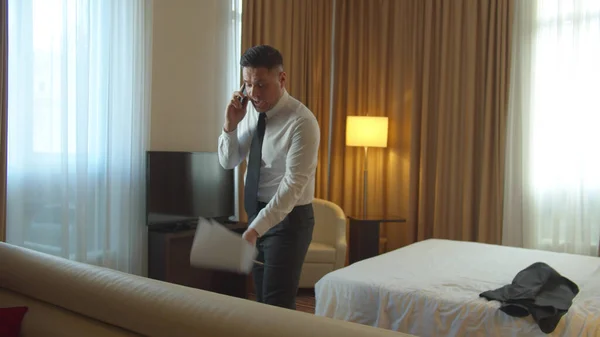 Mann mit Dokumenten in der Hand betritt Hotelzimmer, telefoniert sehr emotional — Stockfoto