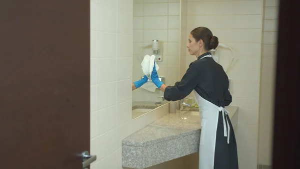 Cameriera in guanti pulire lo specchio in bagno in hotel — Foto Stock