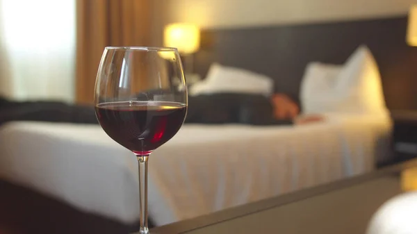 Зосередьтеся на келиху вина в номері готелю, чоловік у костюмі спить на ліжку — стокове фото