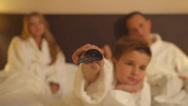 Familie im Hotelzimmer, Eltern sitzen im Bett und Sohn schaltet Fernsehkanäle ein — Stockfoto