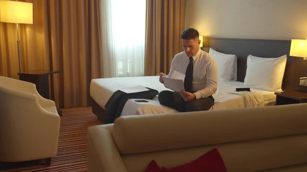 Mann in Hemd und Krawatte sitzt im Hotel auf dem Bett und schreibt auf Papier — Stockfoto