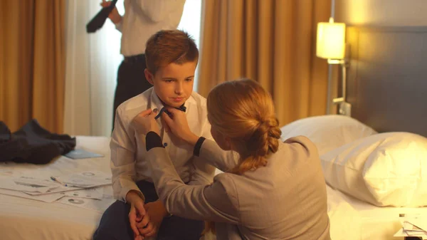 Mutter legte Manschettenknöpfe auf Jungen, die auf dem Bett im Hotel sitzen, Mann zog Jacke an — Stockfoto