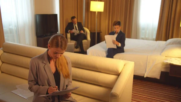 Άνδρας, αγόρι και γυναίκα με κοστούμια κάθονται και εργάζονται με έγγραφα στο δωμάτιο του ξενοδοχείου — Φωτογραφία Αρχείου