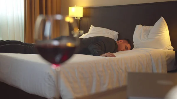 Uomo in tuta dormire in camera d'albergo sullo sfondo di un bicchiere di vino — Foto Stock