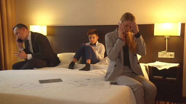 Άντρας και γυναίκα μιλάνε στα τηλέφωνα στο δωμάτιο του ξενοδοχείου, αγόρι κάθεται στο κρεβάτι και ακούει — Φωτογραφία Αρχείου