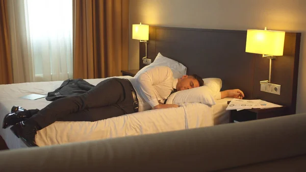 Empresário senta-se na cama e vai dormir no quarto de hotel — Fotografia de Stock