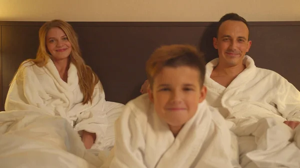 Rodzina w pokoju hotelowym, rodzice siedzieć na łóżku i syn przełącznik chanels na TV — Zdjęcie stockowe