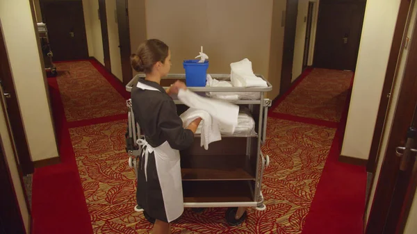 Pokojská vzít ručníky a úklidové vybavení v chodbě hotelu — Stock fotografie