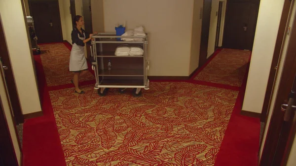 Cameriera uscire dalla camera d'albergo in corridoio con attrezzature per la pulizia — Foto Stock