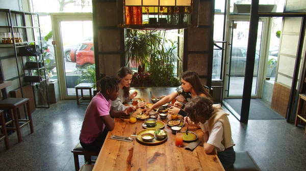 Companhia de amigos se encontram em um café, eles se sentam e comem comida — Fotografia de Stock