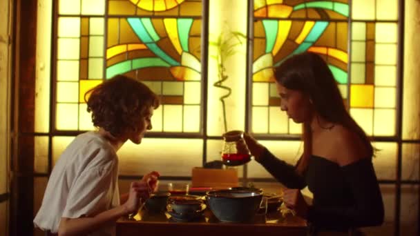 Zeitlupe, Frauen sitzen an einem Tisch in einem Café, Mädchen gießen Tee in Tassen, ein anderes Mädchen spricht — Stockvideo