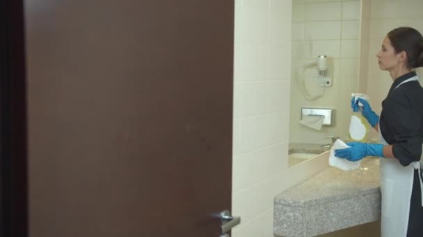 Hembiträde i handskar torka spegeln i badrummet på hotellet — Stockvideo