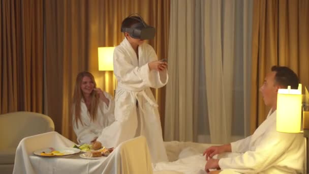 Сім'я в готельному номері, маленький син грає з окулярами віртуальної реальності — стокове відео