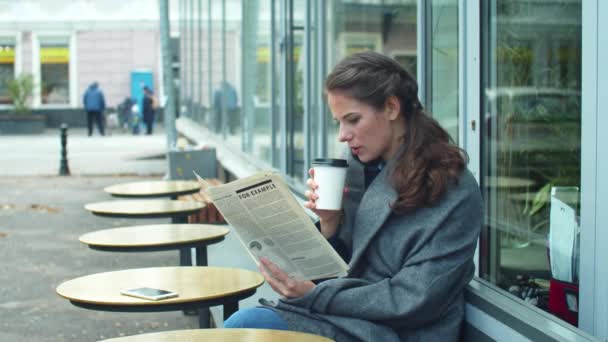 Вид сбоку на девушку в сером одеяле, читающую газету в кафе — стоковое видео