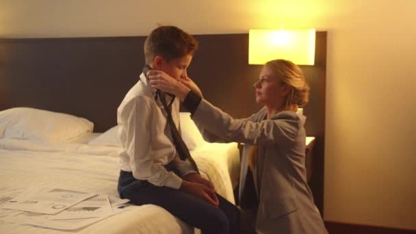 Frau legt Krawatte auf kleinen Jungen, der im Hotel auf dem Bett sitzt
