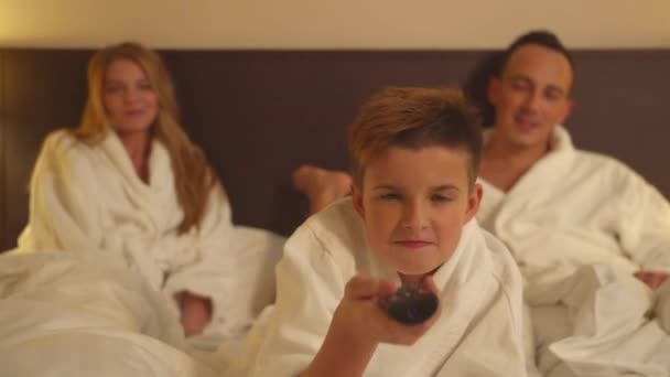 Family in hotel room, parents sit on bed and son switch chanels on TV — Stock Video