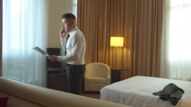 Elinde evrakları olan bir adam otelde yürüyor, telefonda çok duygusal konuşuyor.