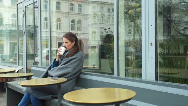 Meisje in grijze deken zitten buiten en drinken koffie — Stockvideo