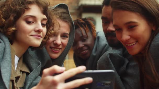 Cámara lenta, amigos en mantas sentarse fuera de la cafetería y mirar la foto en el teléfono — Vídeos de Stock