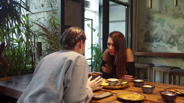 Duas raparigas ao almoço, sentam-se e falam umas com as outras a saborear — Vídeo de Stock