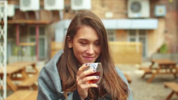 Девушка в сером одеяле пьет горячий чай и смотрит в камеру. — стоковое видео