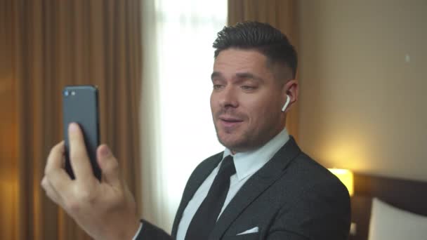 Hombre de chaqueta hablar por teléfono con auriculares en la habitación del hotel — Vídeos de Stock