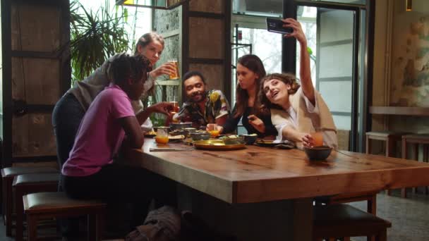 Zwolniony ruch, przyjaciele siedzą w kawiarni, dziewczyna robi zdjęcie grupowe — Wideo stockowe