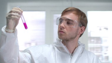 Laboratuvarda koruyucu iş giysisi tüpü ve kimyasal madde kullanan bilim adamları var.