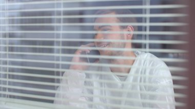 Koruyucu iş kıyafetleri içinde genç bir adam telefonda konuşuyor ve laboratuvarda gülüyor.