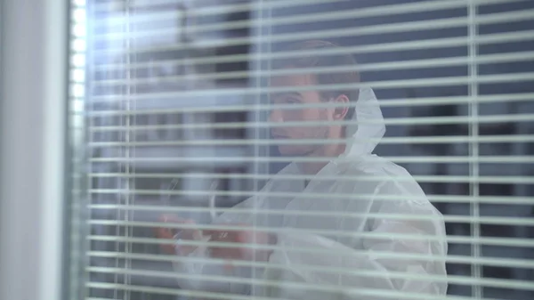 Vista a través de la ventana, el hombre se puso ropa de trabajo protectora blanca —  Fotos de Stock