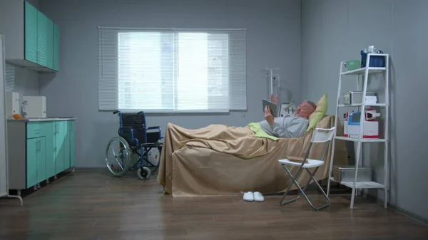 Man ligt op het bed in het ziekenhuis en praat met iemand op tablet — Stockfoto