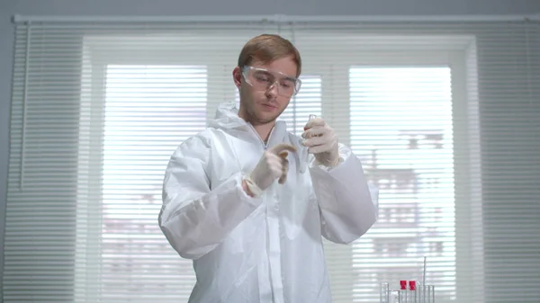 Ученый в защитной рабочей одежде и перчатках наливает что-то в трубку в лаборатории — стоковое фото