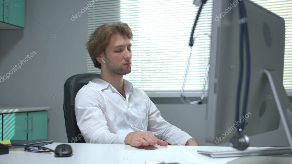 Doctor sits at a table with his eyes closed and listens music wearing headphones 