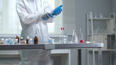 Koruyucu iş kıyafetli bir adam laboratuarda tıbbi eldiven takmış.