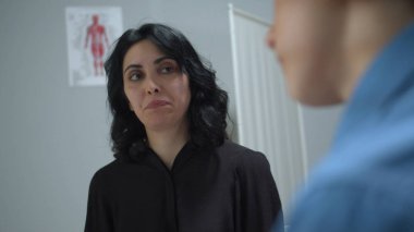 Çocuk annesiyle oturur ve hastane kabinesinde doktorla konuşur.