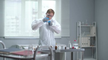 Yavaş çekim, koruyucu giyimli ve tıbbi eldivenli adam laboratuarda tüpü aç.
