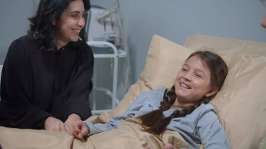 Anne ve diğer akrabalar hastanede yatakta yatan kızla konuşuyorlar.